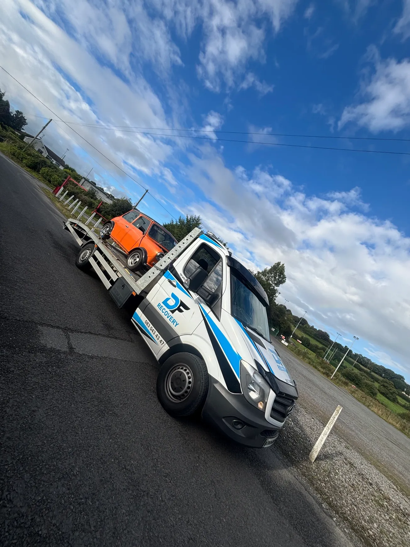 DF Recovery truck transporting a classic orange Mini on a country road.
