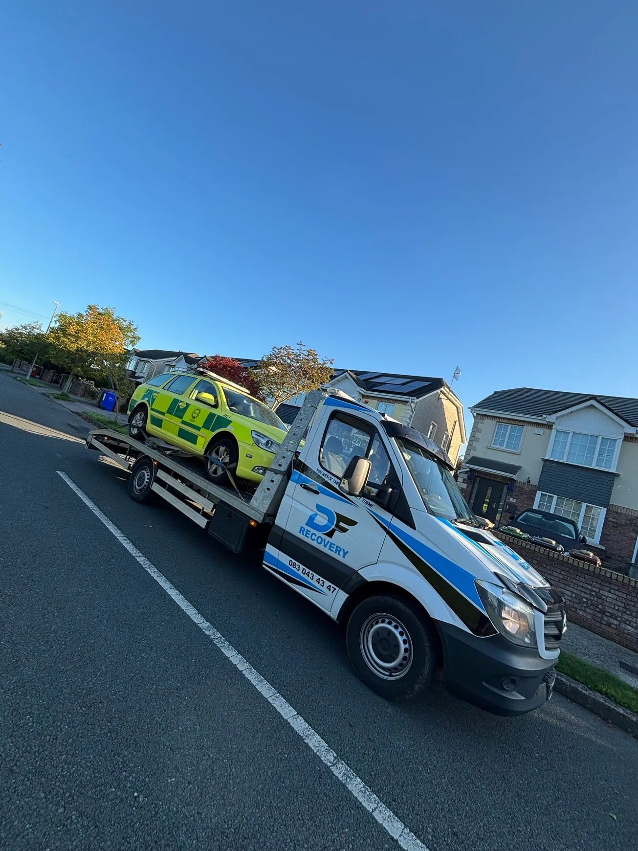 DF Recovery truck carrying a high-visibility response car under a clear blue sky.